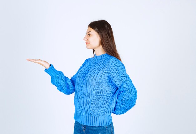 Retrato de uma menina adolescente de suéter azul em pé e sorrindo alegremente.