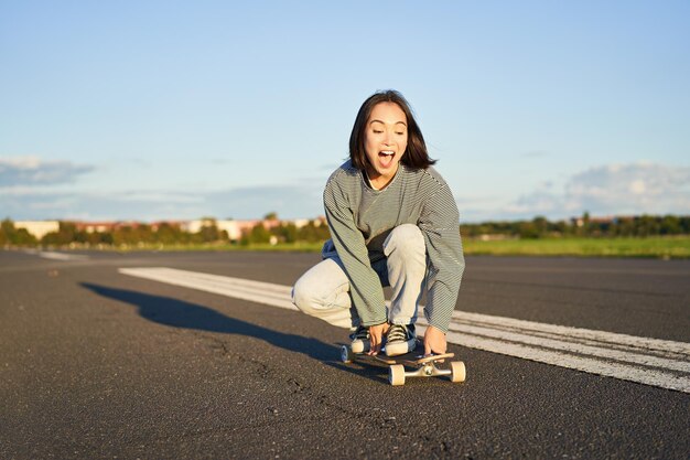 Retrato de uma menina asiática feliz e despreocupada patinando andando de skate e rindo aproveitando o dia ensolarado