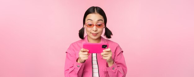 Retrato de uma menina asiática feliz jogando no smartphone assistindo vídeos no aplicativo de celular em pé