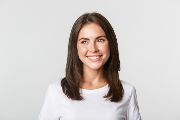 Retrato de uma menina atraente pensativa sorrindo e olhando para a esquerda, branco.