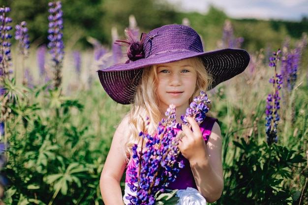 Retrato de uma menina bonita com um chapéu violeta com buquês de tremoços no rosto