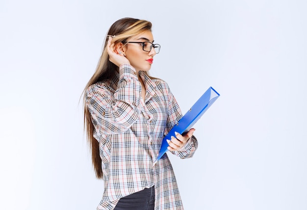 Retrato de uma menina bonita de óculos em pé, posando com uma pasta.