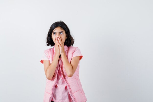 Retrato de uma menina com camiseta branca e colete bufê cobrindo a boca