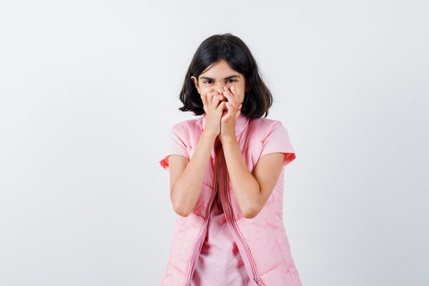 Retrato de uma menina com camiseta branca e colete bufê cobrindo a boca