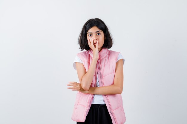 Retrato de uma menina com camiseta branca e colete bufê cobrindo a boca