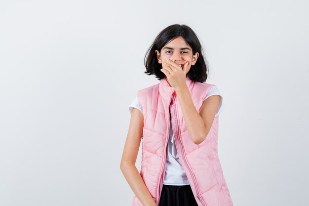 Retrato de uma menina com camiseta branca e colete bufê cobrindo a boca