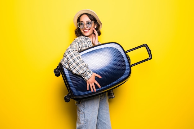 Foto grátis retrato de uma menina com chapéu de palha e óculos escuros com mala isolada sobre parede amarelo dourado