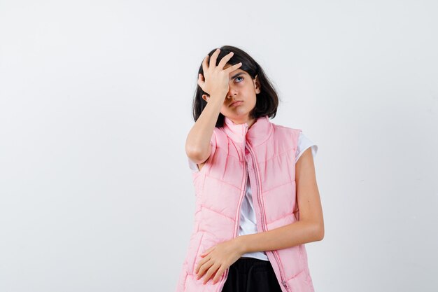 Retrato de uma menina em camiseta branca e colete bufê colocando a mão na cabeça