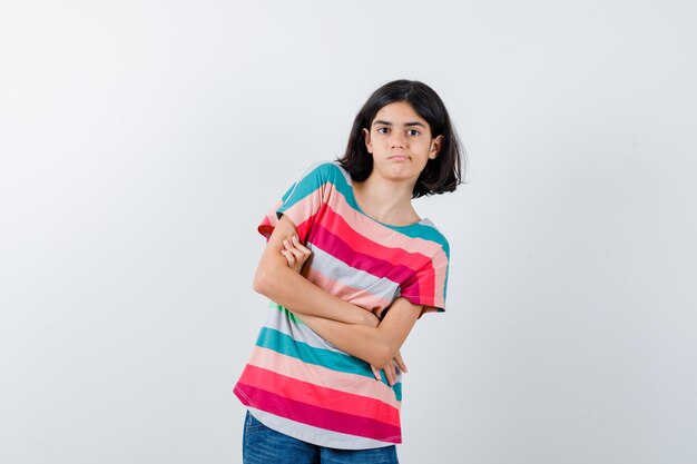 Retrato de uma menina em pé com os braços cruzados na camiseta e olhando de frente hesitante