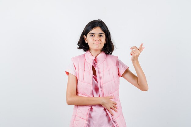 Retrato de uma menina em uma camiseta branca e colete bufê apontando para o lado