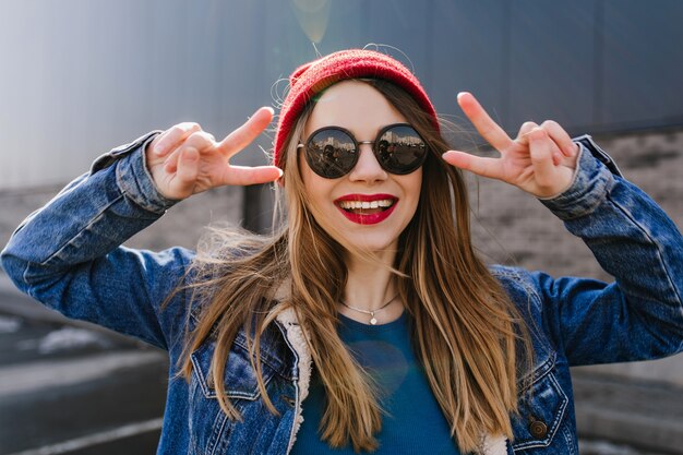 Retrato de uma menina feliz com cabelo liso claro rindo. Foto de alegre mulher branca de óculos, posando na rua em um dia ensolarado.