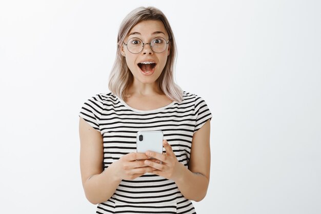 Retrato de uma menina loira animada posando no estúdio com seu telefone