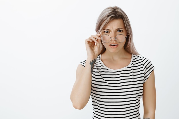 Retrato de uma menina loira insegura de óculos, posando no estúdio