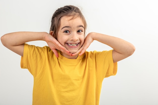 Retrato de uma menina mantendo as mãos perto do rosto sorrindo isolada em branco