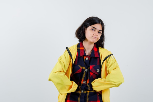 Retrato de uma menina segurando os punhos na barriga com uma camisa quadrada, jaqueta e olhando confiante para a frente