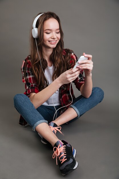 Retrato de uma menina sorridente, ouvindo música no telefone