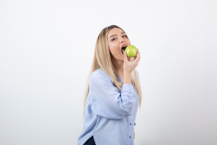Foto grátis retrato de uma modelo de menina bonita em pé e comendo uma maçã verde fresca.