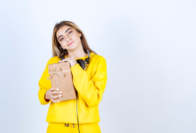 Retrato de uma modelo de menina segurando uma caixa de papel com um laço isolado na parede branca