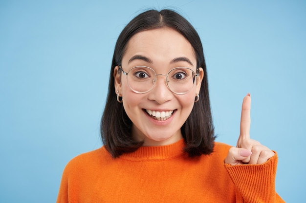 Foto grátis retrato de uma morena asiática sorridente em óculos levanta um dedo sinal de eureca lançando uma ideia h