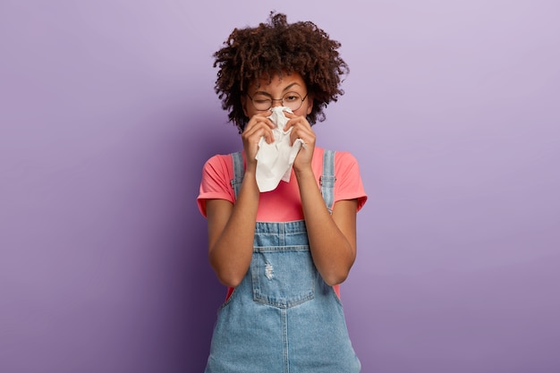 Foto grátis retrato de uma mulher afro-americana doente espirra no tecido branco, sofre de rinite e coriza