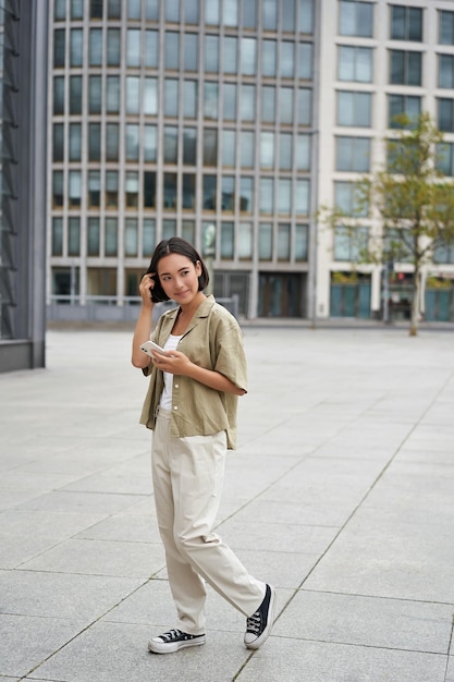 Foto grátis retrato de uma mulher asiática andando no estilo de rua da cidade, tiro de menina com smartphone posando ao ar livre em