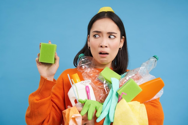 Foto grátis retrato de uma mulher asiática com nojo de uma esponja suja segurando garrafas vazias recicláveis