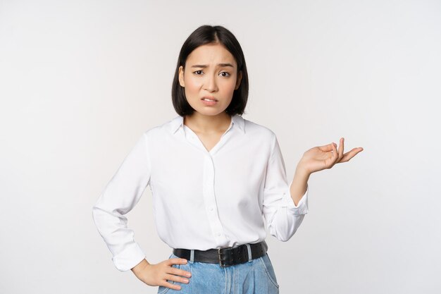Retrato de uma mulher asiática confusa perguntando qual é o seu gesto de problema olhando intrigado sem noção e irritado em pé sobre fundo branco
