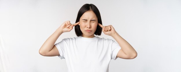 Retrato de uma mulher asiática fechando os ouvidos e sentindo desconforto com o som irritante do barulho alto sobre fundo branco