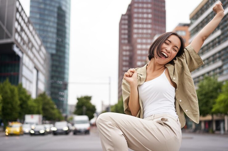 Foto grátis retrato de uma mulher asiática feliz dançando e sentindo alegria triunfando levantando a mão em gesto de vitória