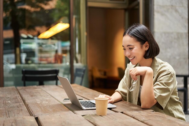 Retrato de uma mulher asiática olhando para o bate-papo por vídeo do laptop conversando com alguém via câmera de computador sentada