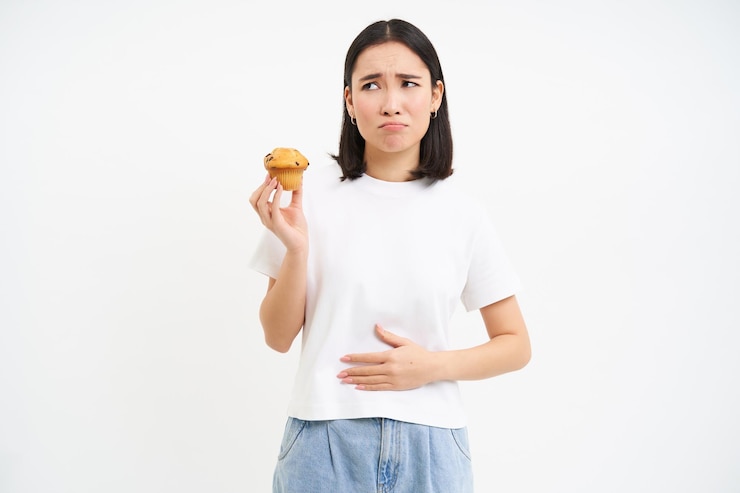 Foto grátis retrato de uma mulher asiática sentindo dor no desconforto estomacal após comida segurando cupcake e olhando un