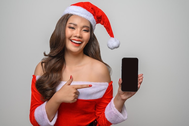 Retrato de uma mulher asiática sorridente com fantasia de Papai Noel vermelho posando com smartphone