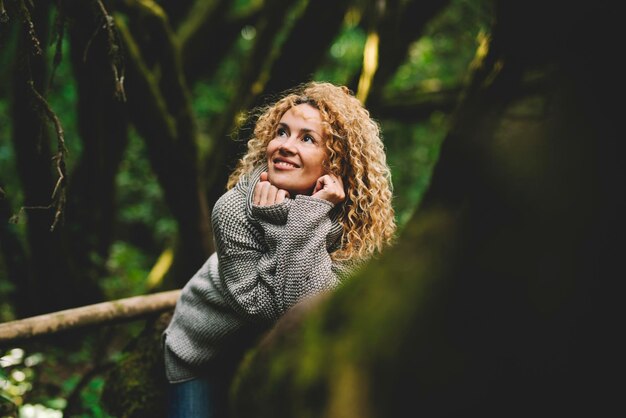 Retrato de uma mulher atraente caucasiana, sorrindo e apreciando a floresta verde floresta ao ar livre. pessoas e viagens de estilo de vida ambiental da natureza. lindo sorriso feminino deitado em um tronco de árvore