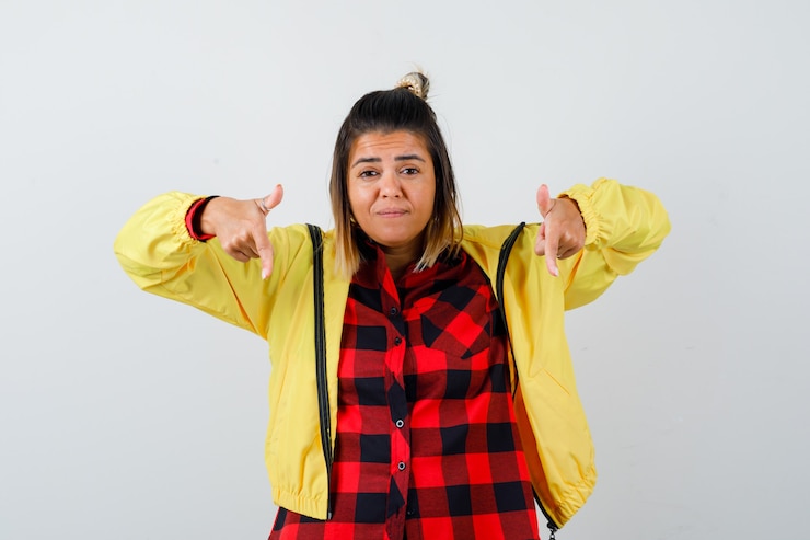 Foto grátis retrato de uma mulher bonita apontando para baixo em uma camisa, jaqueta e parecendo indeciso com a vista frontal