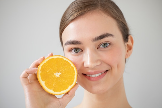 Retrato de uma mulher bonita com pele clara segurando fatias de frutas de laranja