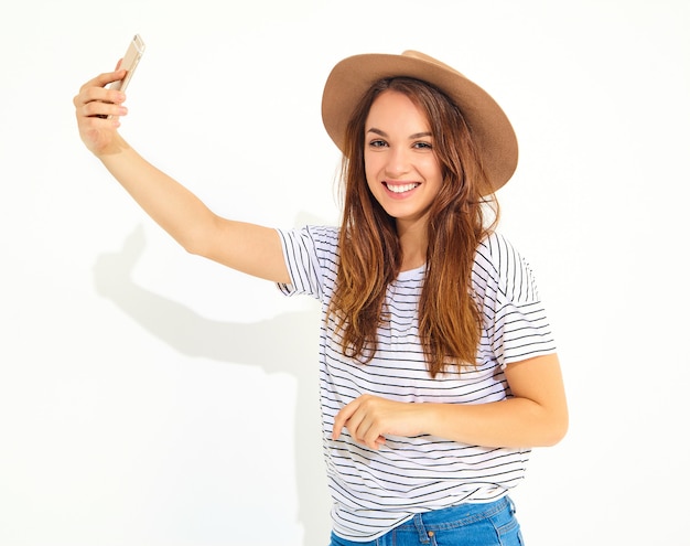 Retrato de uma mulher bonita em roupas de verão hipster tomando uma selfie isolada na parede branca