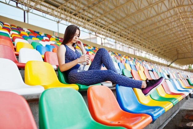 Retrato de uma mulher bonita em roupas esportivas sentada e bebendo água no estádio