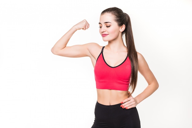 Retrato de uma mulher bonita fitness mostrando seu bíceps em uma parede branca