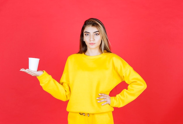 Retrato de uma mulher bonita segurando uma xícara de chá de plástico na parede vermelha