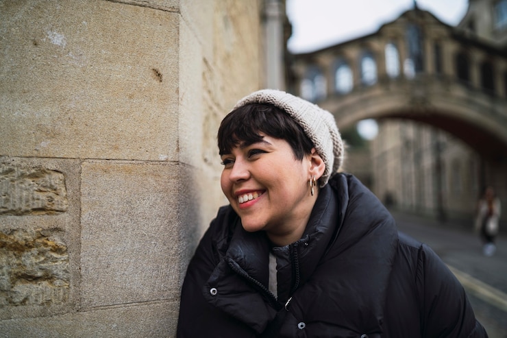 Foto grátis retrato de uma mulher branca e sorridente atraente, com um chapéu e um casaco encostado na parede