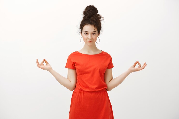 Foto grátis retrato de uma mulher caucasiana calma e bonita com cabelo encaracolado, estendendo as mãos em um gesto zen e sorrindo com expressão intrigada, relaxante