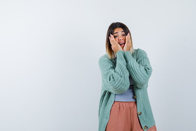 Retrato de uma mulher com as mãos no rosto em roupas casuais e olhando animada para a frente