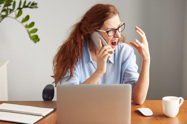 Retrato de uma mulher de negócios zangada de óculos gritando ao telefone