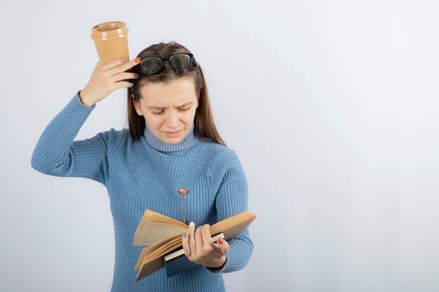 Retrato de uma mulher de óculos, lendo um livro com uma xícara de café.