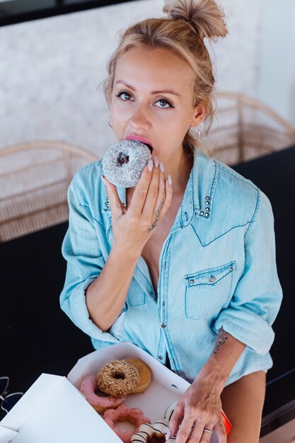 Retrato de uma mulher Europeia com cabelo loiro, desfrutando de donuts na cozinha em casa villa.