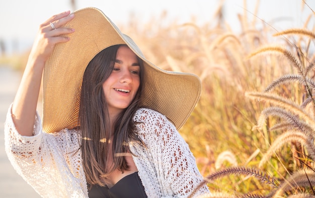 Retrato de uma mulher feliz ao sol, sentada em um campo, vestida com roupas de verão e um chapéu.