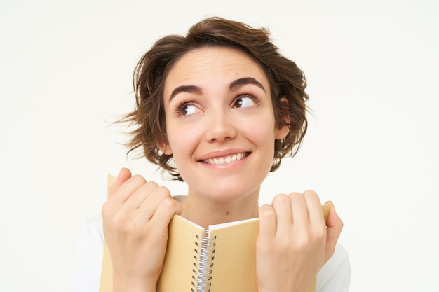 Foto grátis retrato de uma mulher feliz com planejador segurando notas de leitura de caderno e sorrindo em pé sobre branco