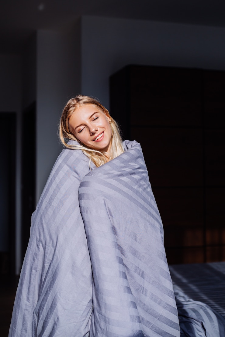 Foto grátis retrato de uma mulher feliz e calma no quarto com um cobertor cinza despojado e um corpo preto e bege, roupa de dormir em casa