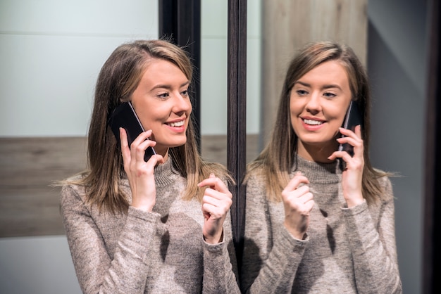 Retrato de uma mulher feliz olhando seu reflexo no espelho e falando ao telefone. Rapariga sexy chamada por telefone