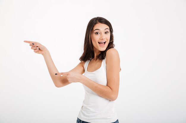 Retrato de uma mulher feliz, vestida com os dedos apontando para a parte superior do tanque